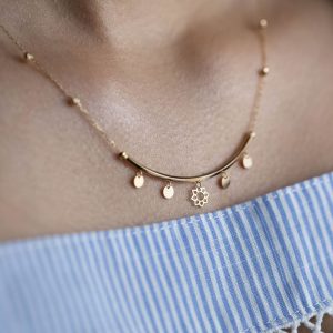 Close-up of a delicate gold necklace worn on a striped dress, showcasing intricate design.