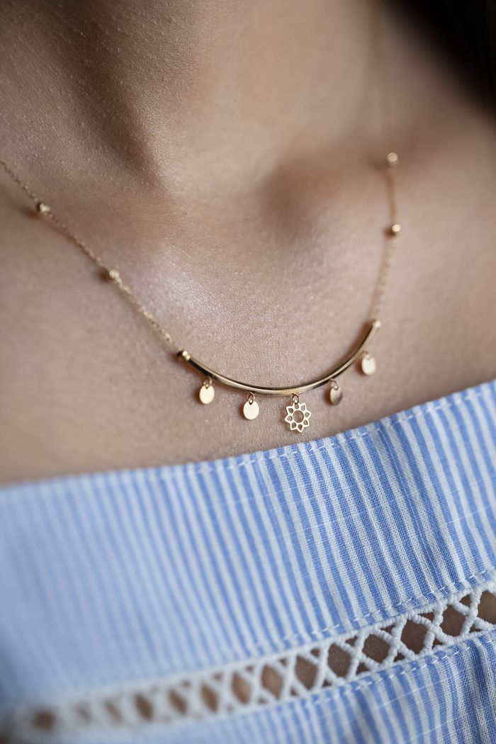 Close-up of a delicate gold necklace worn on a striped dress, showcasing intricate design.